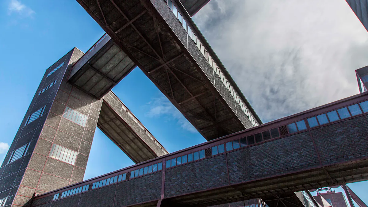 Das Bild zeigt eine ungewöhnliche Perspektive auf die Architektur der Zeche Zollverein, aufgenommen von unten mit Blick auf die Bandbrücken rund um die Kohlenwäsche. Die massiven Backsteinbauten und die dunklen Stahlträger kontrastieren mit dem hellblauen Himmel und den vorbeiziehenden Wolken. Diese dynamische, fast abstrakte Komposition hebt die geometrischen Strukturen der ehemaligen Industrieanlage hervor und bietet den Betrachtern eine völlig neue Sichtweise auf die beeindruckende Architektur. Perspektiven wie diese laden Besucher und Fotografen dazu ein, das UNESCO-Welterbe Zollverein aus immer neuen Blickwinkeln zu entdecken.