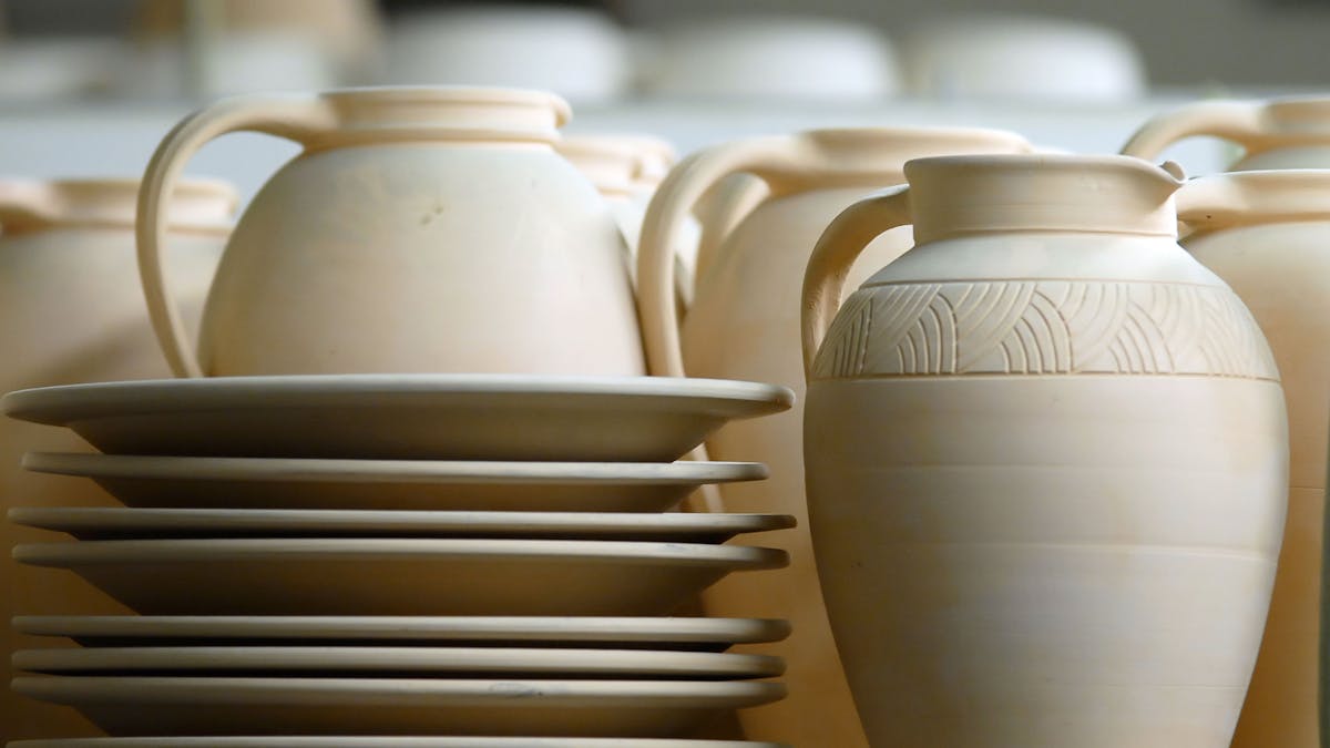 Handgefertigte Keramik von Young-Jae Lee in der Keramischen Werkstatt Margaretenhöhe. Zu sehen sind detailreich gestaltete, unglasierte Teller und Krüge in warmen, natürlichen Farbtönen. Die Stücke zeichnen sich durch präzise Formen und feine Gravuren aus. Die Werkstatt Margaretenhöhe ist bekannt für ihre traditionelle Handwerkskunst, die auf Zollverein produziert wird.