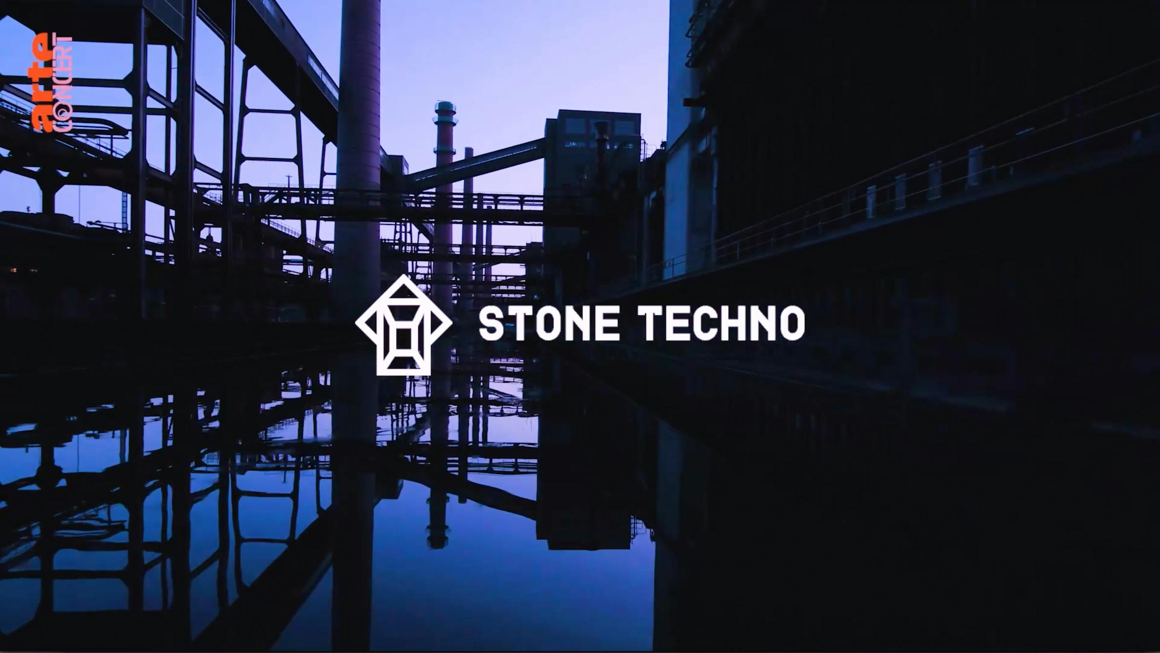 Industrieanlage bei Dämmerung mit reflektierenden Wasserflächen im Vordergrund. In der Bildmitte befindet sich ein stilisiertes weißes Logo mit geometrischen Formen, daneben steht der Schriftzug Stone Techno in Großbuchstaben. In der oberen linken Ecke ist das Logo von Arte Concert in orange und weiß zu sehen. Die Szenerie wirkt atmosphärisch und industriell.