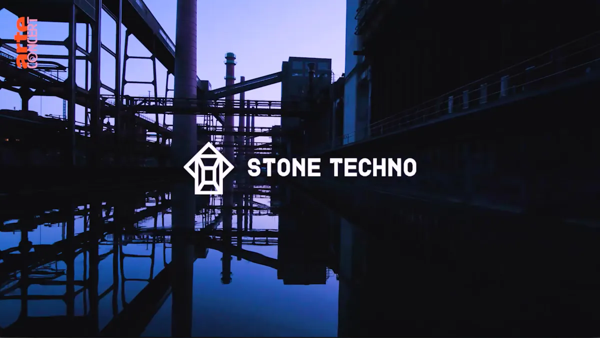 Industrieanlage bei Dämmerung mit reflektierenden Wasserflächen im Vordergrund. In der Bildmitte befindet sich ein stilisiertes weißes Logo mit geometrischen Formen, daneben steht der Schriftzug Stone Techno in Großbuchstaben. In der oberen linken Ecke ist das Logo von Arte Concert in orange und weiß zu sehen. Die Szenerie wirkt atmosphärisch und industriell.