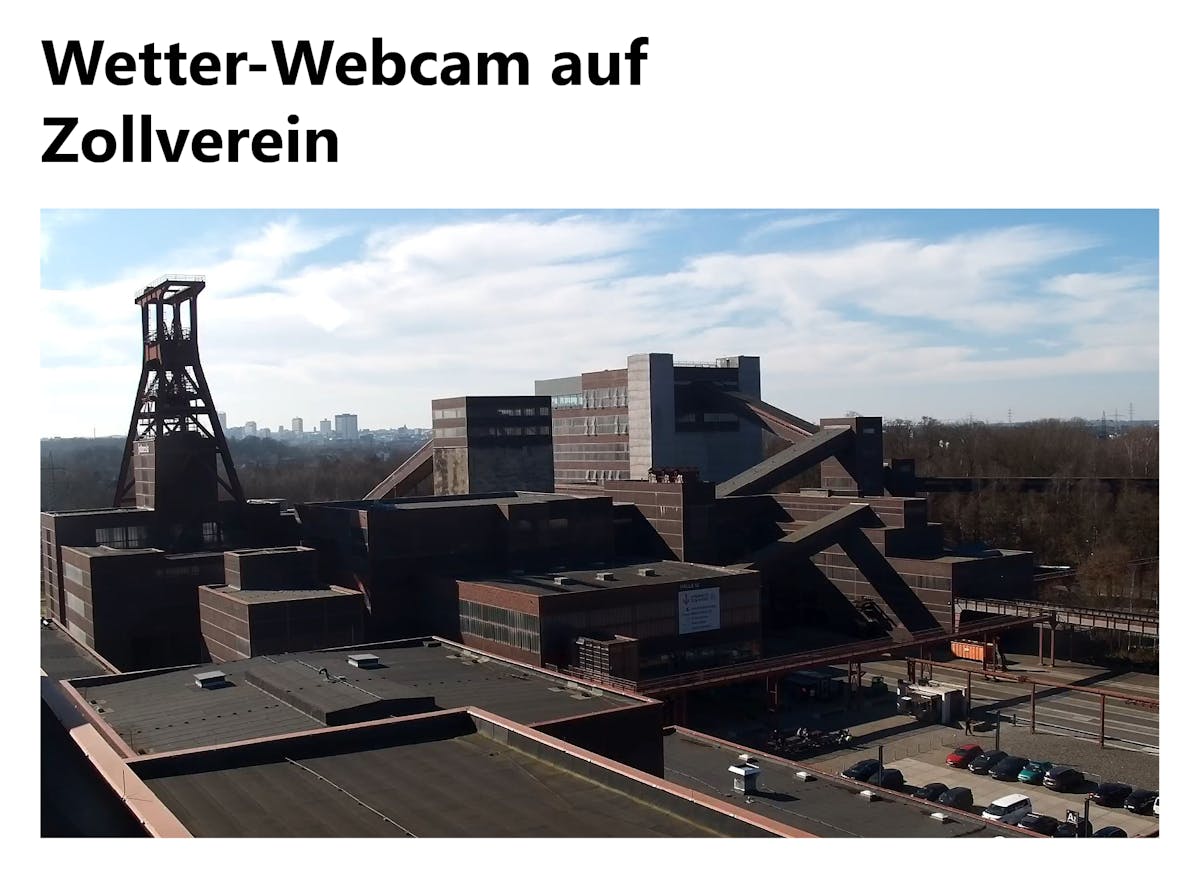 Das Bild zeigt eine Webcam-Aufnahme des UNESCO-Welterbes Zeche Zollverein in Essen bei Tageslicht. Im Vordergrund sind die markanten Backstein-Industriebauten mit ihren klaren geometrischen Formen zu sehen. Links ragt das berühmte Doppelbock-Fördergerüst in den Himmel. Im Hintergrund erstreckt sich die Skyline von Essen mit Hochhäusern am Horizont, dahinter ein klarer Himmel mit leichten Wolken. Unten rechts sind parkende Autos und ein Eingangsbereich zu erkennen. Oben im Bild steht der Titel Wetter-Webcam auf Zollverein in schwarzer Schrift auf weißem Hintergrund.
