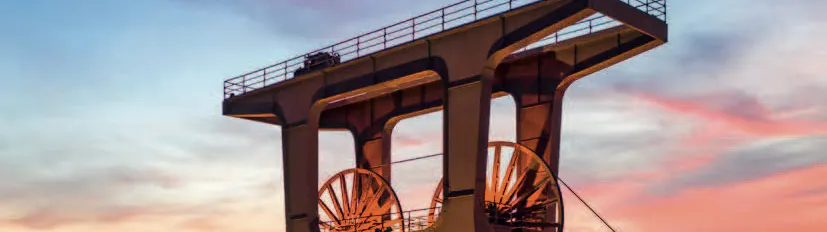 Titelseite eines Sales Guides für das UNESCO-Welterbe Zollverein. Im Vordergrund steht der Förderturm der Zeche Zollverein bei Sonnenuntergang, warm beleuchtet vor einem blau-orangefarbenen Himmel. Oben rechts sind das Logo von Zollverein und der Hinweis auf 25 Jahre UNESCO-Welterbe zu sehen.
