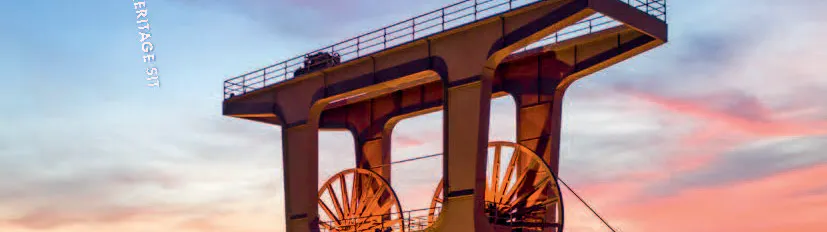 Titelseite eines Sales Guides für das UNESCO World Heritage Site Zollverein. Im Vordergrund ist der markante Förderturm der Zeche Zollverein bei Sonnenuntergang zu sehen, warm beleuchtet vor einem blau-orangefarbenen Himmel. Oben rechts stehen das Zollverein-Logo und der Hinweis auf 25 Jahre UNESCO-Welterbe.